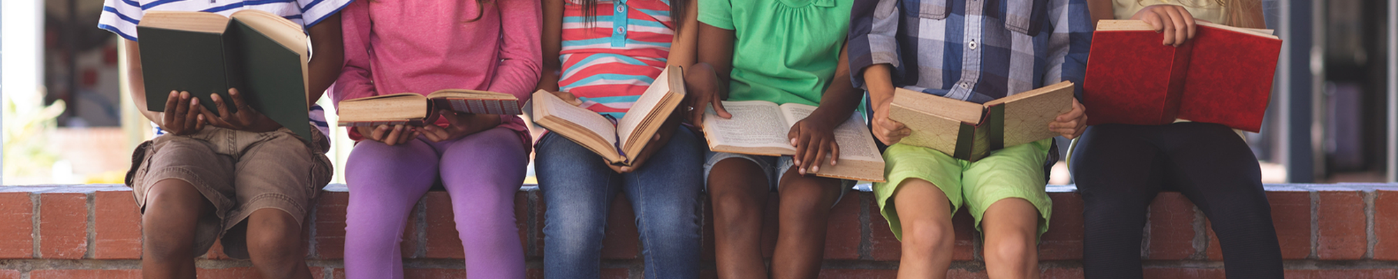 Group of students wearing colorful clothes sitting outside with books 