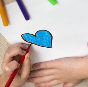 young student's hand drawing a heart on paper