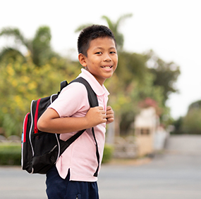 School boy with red backpack looking back for a pic outside